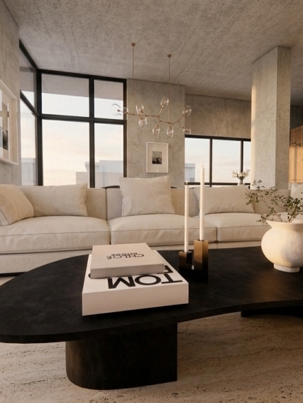 Contemporary interior space with exposed concrete surfaces, windows from floor to ceiling, travertine flooring, off-white sectional sofa and oak kitchen cabinetry in the background. Image copyright: Karydis & Associates.